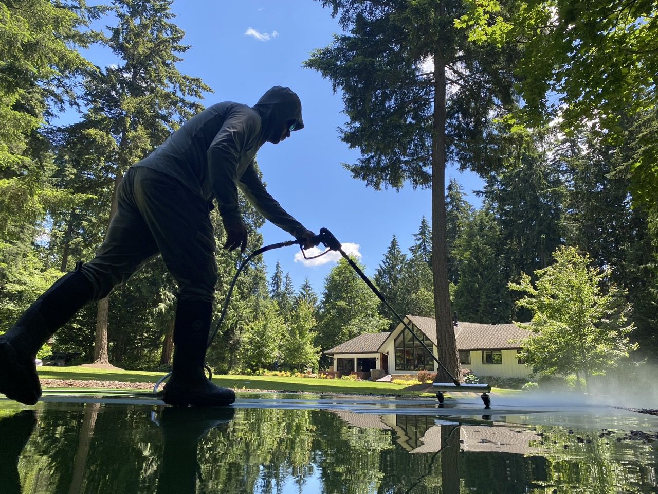 Fuego crew member pressure-washing a stone patio surrounded by evergreens